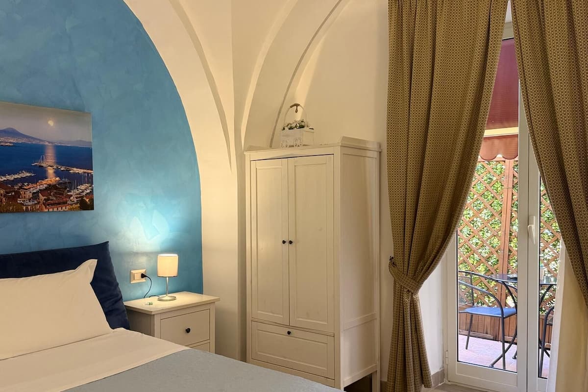 A bedroom with a bed, a nightstand, a wardrobe, and a view of an outdoor patio.