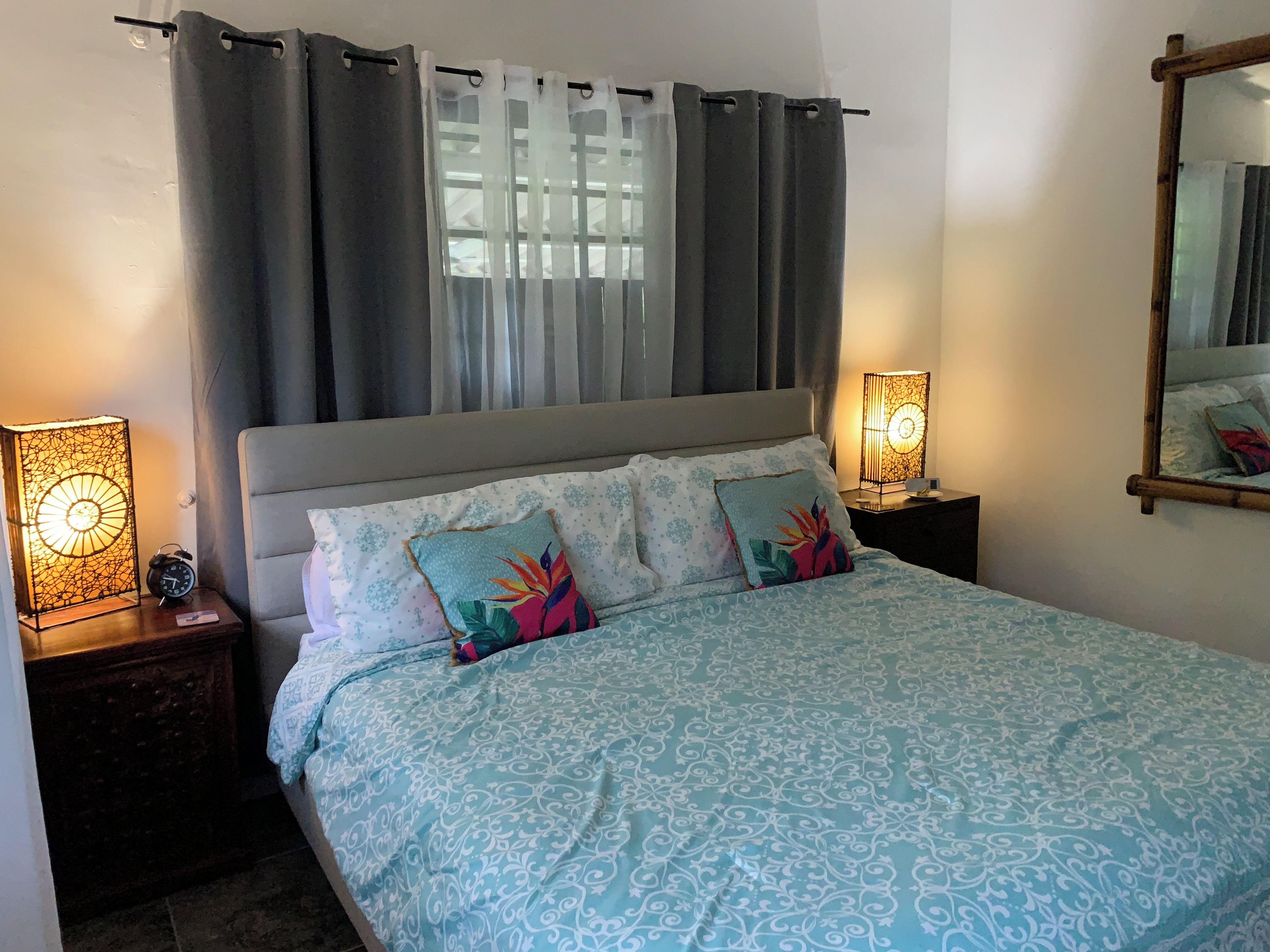 Un dormitorio con una cama, dos lámparas de noche, una mesita de noche, un espejo y una ventana con cortinas.