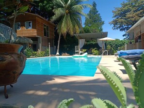 Un área de piscina con sillas de descanso, una estructura de techo de paja y palmeras.