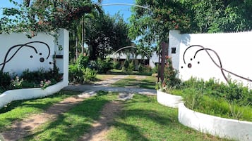 Un camino que lleva a un edificio de paredes blancas y un jardín con diversas plantas y flores.