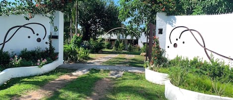 Un camino que lleva a un edificio de paredes blancas y un jardín con diversas plantas y flores.