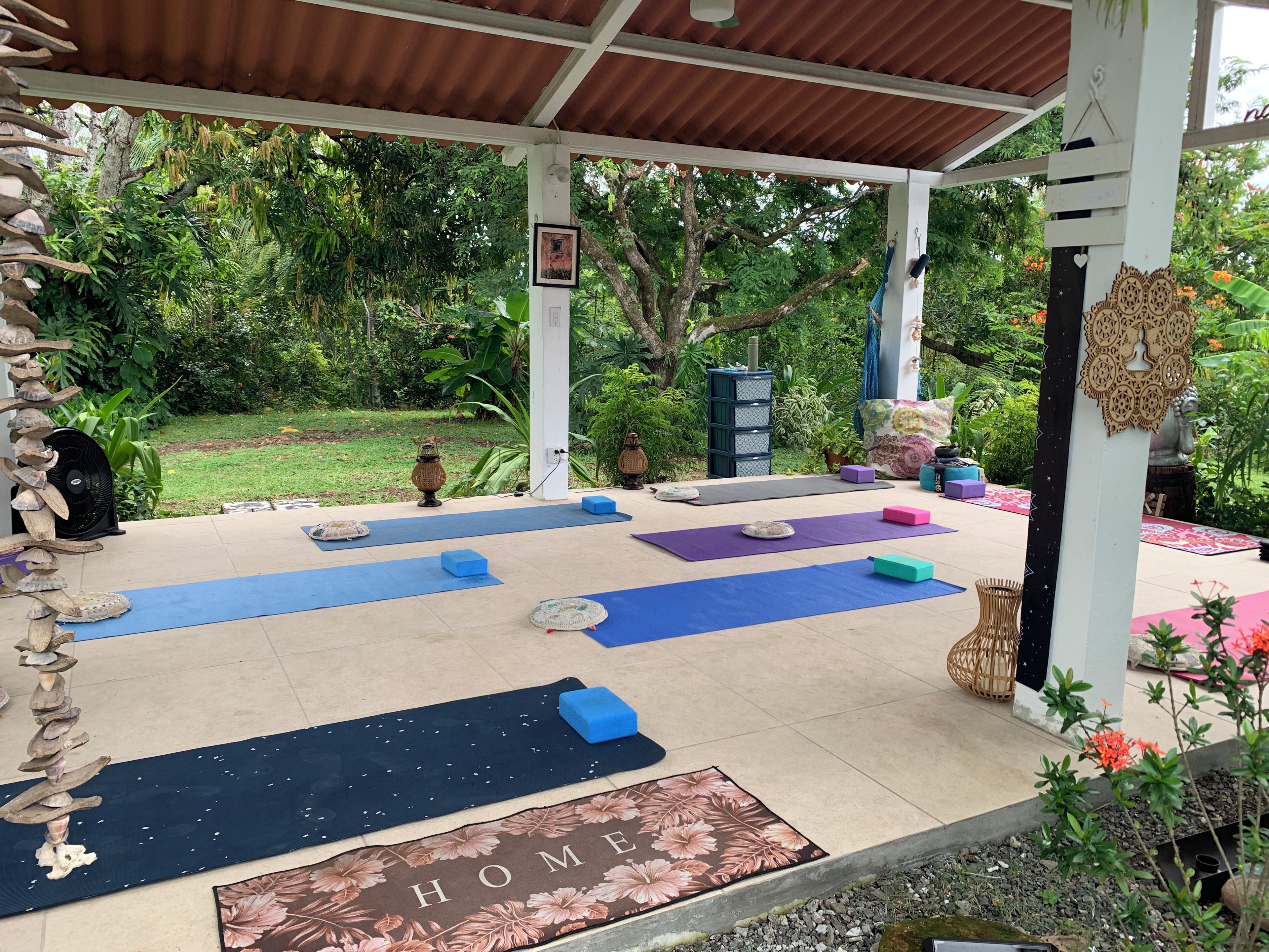 Un espace extérieur abrité, équipé de tapis de sol pour les exercices, d’un tapis portant l’inscription « HOME » et agrémenté d’une structure décorative en bois.
