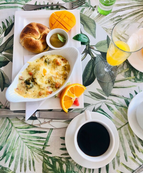 A breakfast setting with a plate of food, a glass of orange juice, a cup of coffee, and a bottle of green drink.
