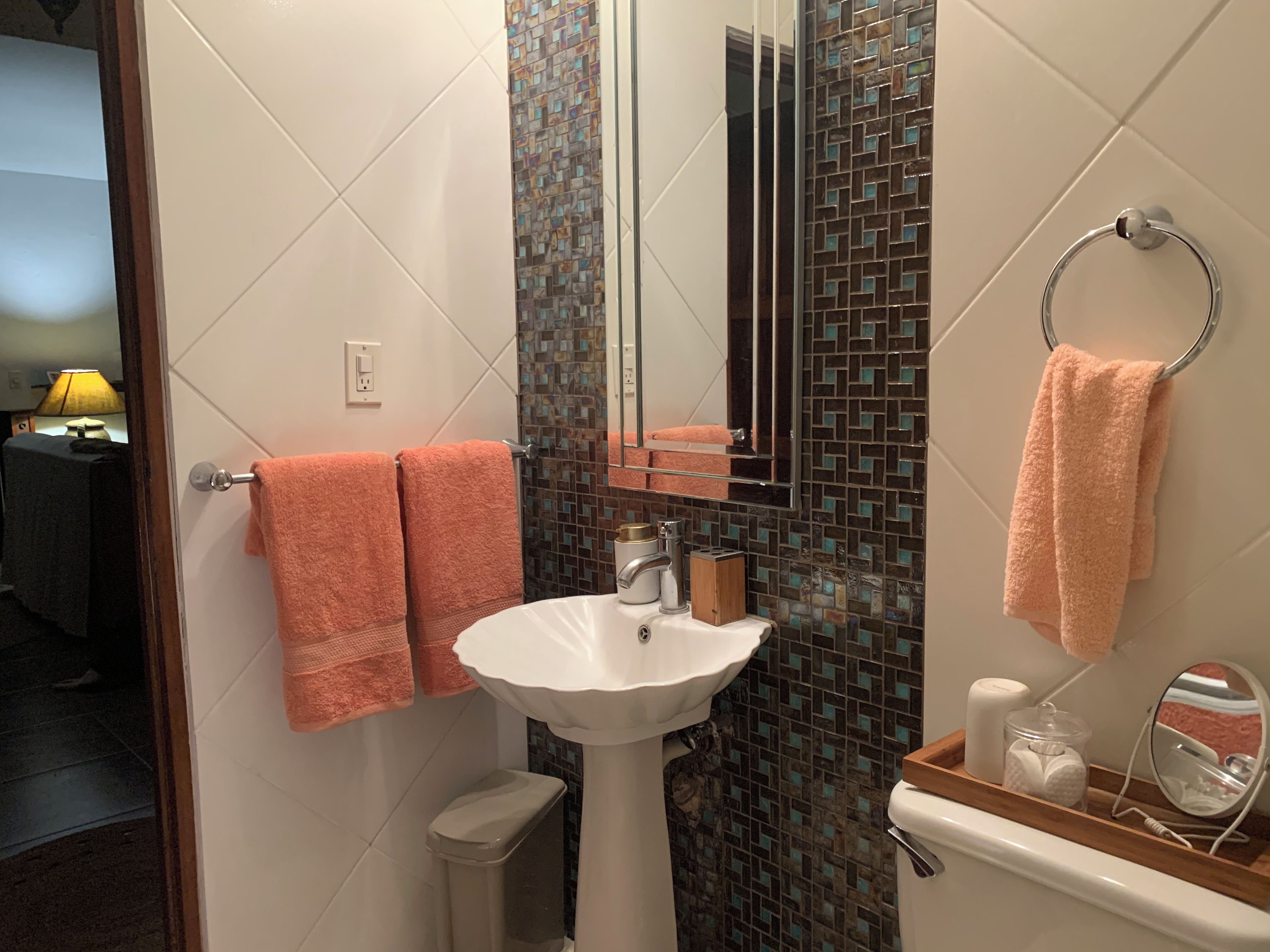 Et badeværelse med hvid vask, et spejl, et håndklædetørrestativ og et toilet.