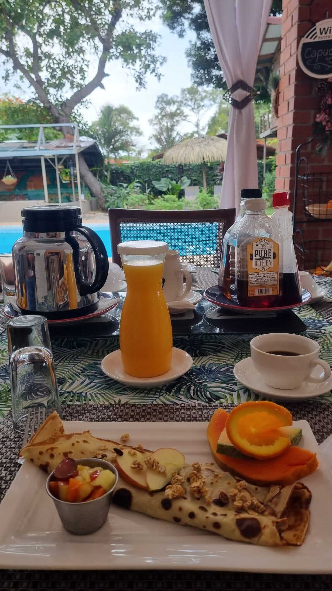 A breakfast setting with a coffee pot, juice, honey, and a plate of food including a rolled pastry and fruit.