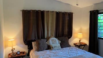 A bedroom with a bed, two bedside tables, a ceiling fan, and a window with curtains.