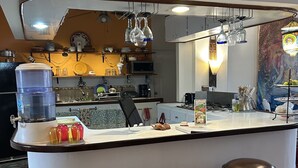 Une cuisine avec un îlot central blanc, deux tabourets, un distributeur d’eau et une horloge au mur.
