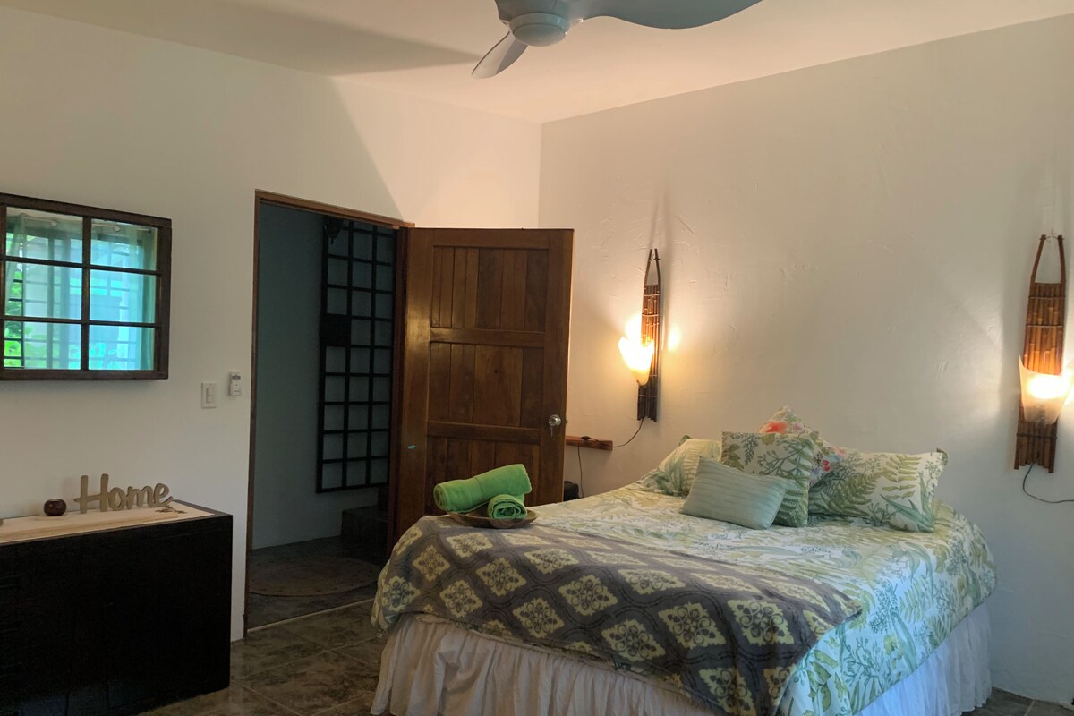 A bedroom with a bed, a wooden door, a window, and a wall-mounted light fixture.