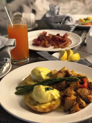 Un desayuno con huevos Benedictinos, tocino y un vaso de jugo de naranja.