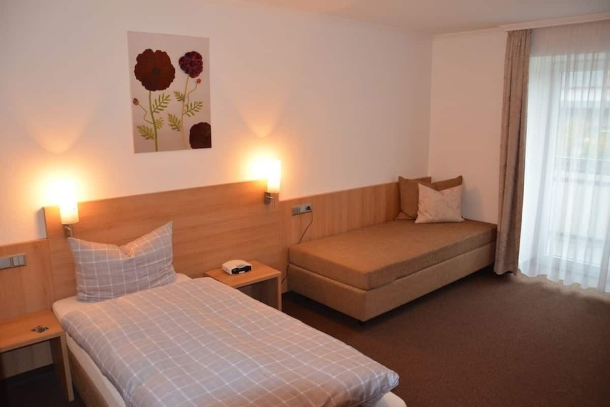 A hotel room with two beds, a sofa, a wall-mounted artwork, and a window with curtains.