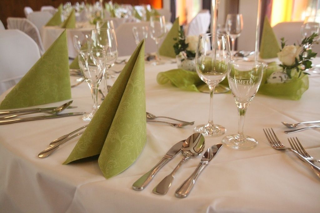 Mesa preparada para un evento de cena formal, con servilletas verdes, cubiertos y copas de vino.