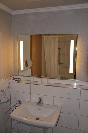 A bathroom with a white sink, a mirror, and a shower. - Gasthof Grofe (Anrochte)
