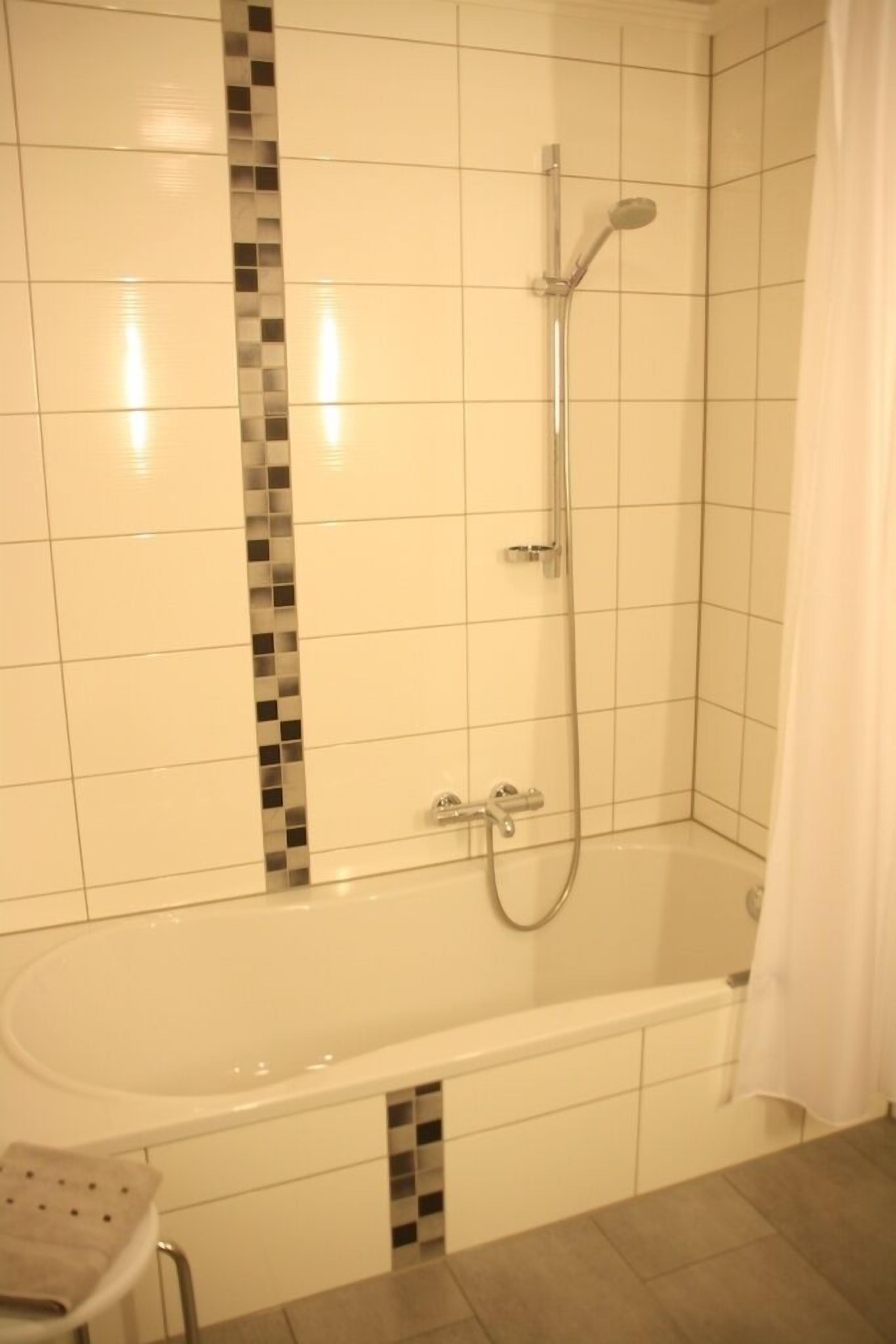 A bathroom with a bathtub, shower, and tiled walls.