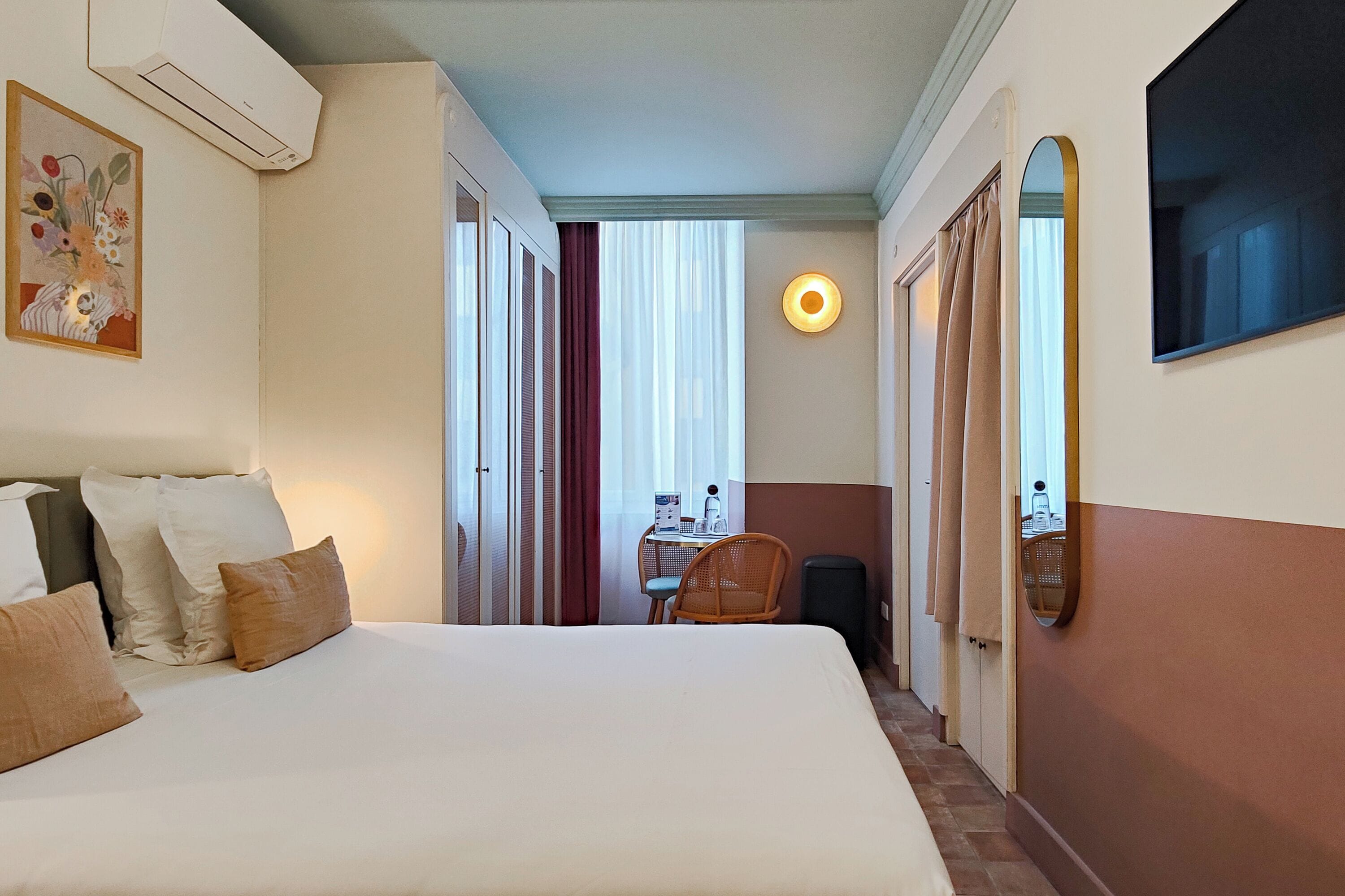 A hotel room with a large bed, a desk with a chair, a mirror, and a window with curtains.