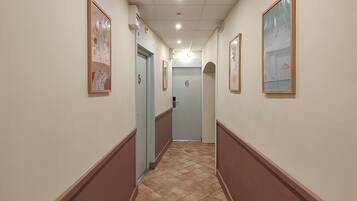 A hallway with numbered doors, framed artwork on the walls, and a tiled floor.