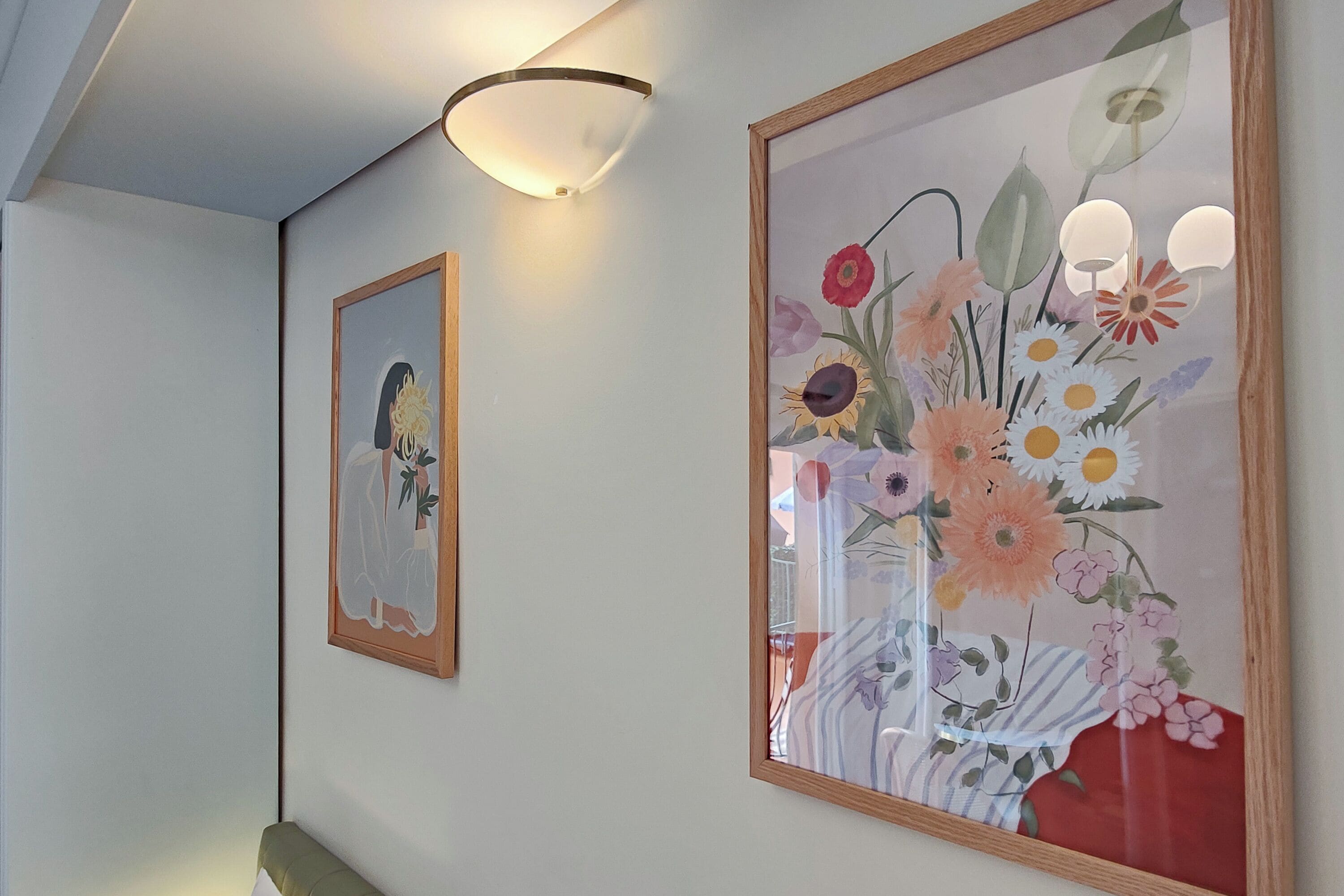 Een hal met twee ingelijste kunstwerken, waarvan één een figuur met een plant toont en de ander een bloemstuk.