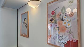 Een hal met twee ingelijste kunstwerken, waarvan één een figuur met een plant toont en de ander een bloemstuk.