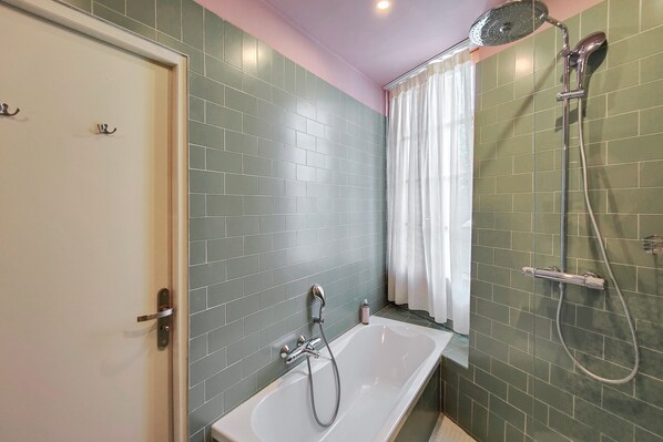 A bathroom with a bathtub, a shower, and a door with hooks. - Hotel Aparthotel AMMI Vieux Nice (Nice)
