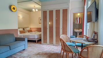 Una habitación con sofá, cama, mesa de comedor con sillas, televisor y baño con lavamanos y espejo.