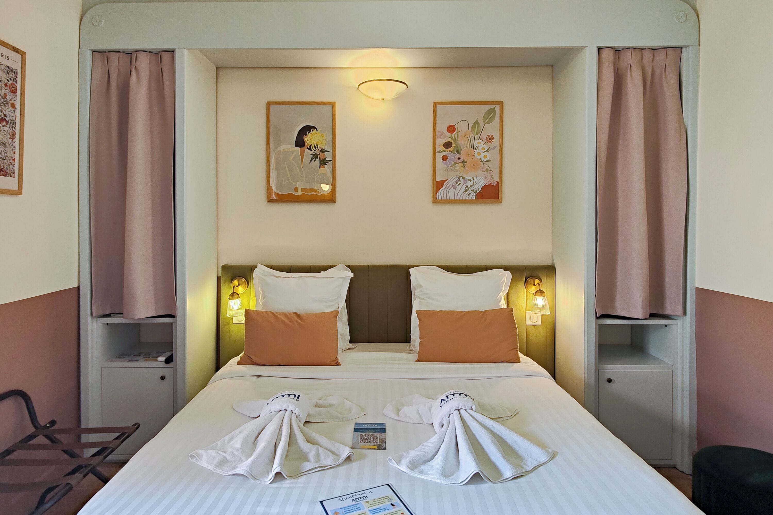 Una habitación de hotel con una cama, dos mesitas de noche, una silla y dos lámparas de pared.