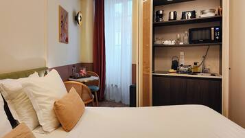 A hotel room with a bed, a small table with chairs, a kitchenette with a microwave, and a window with curtains.