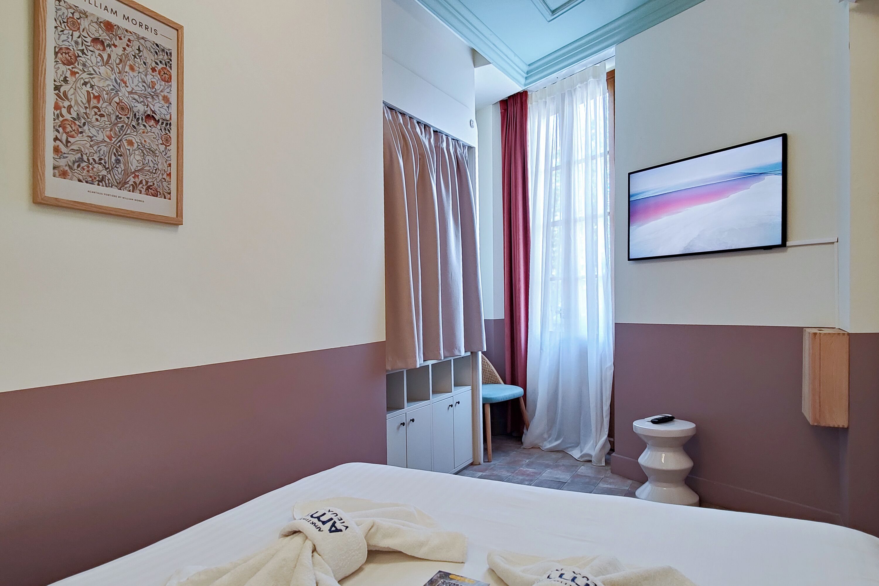 Ein Hotelzimmer mit Bett, Fernseher, Schrank, Toilette und einem Fenster mit Vorhängen.