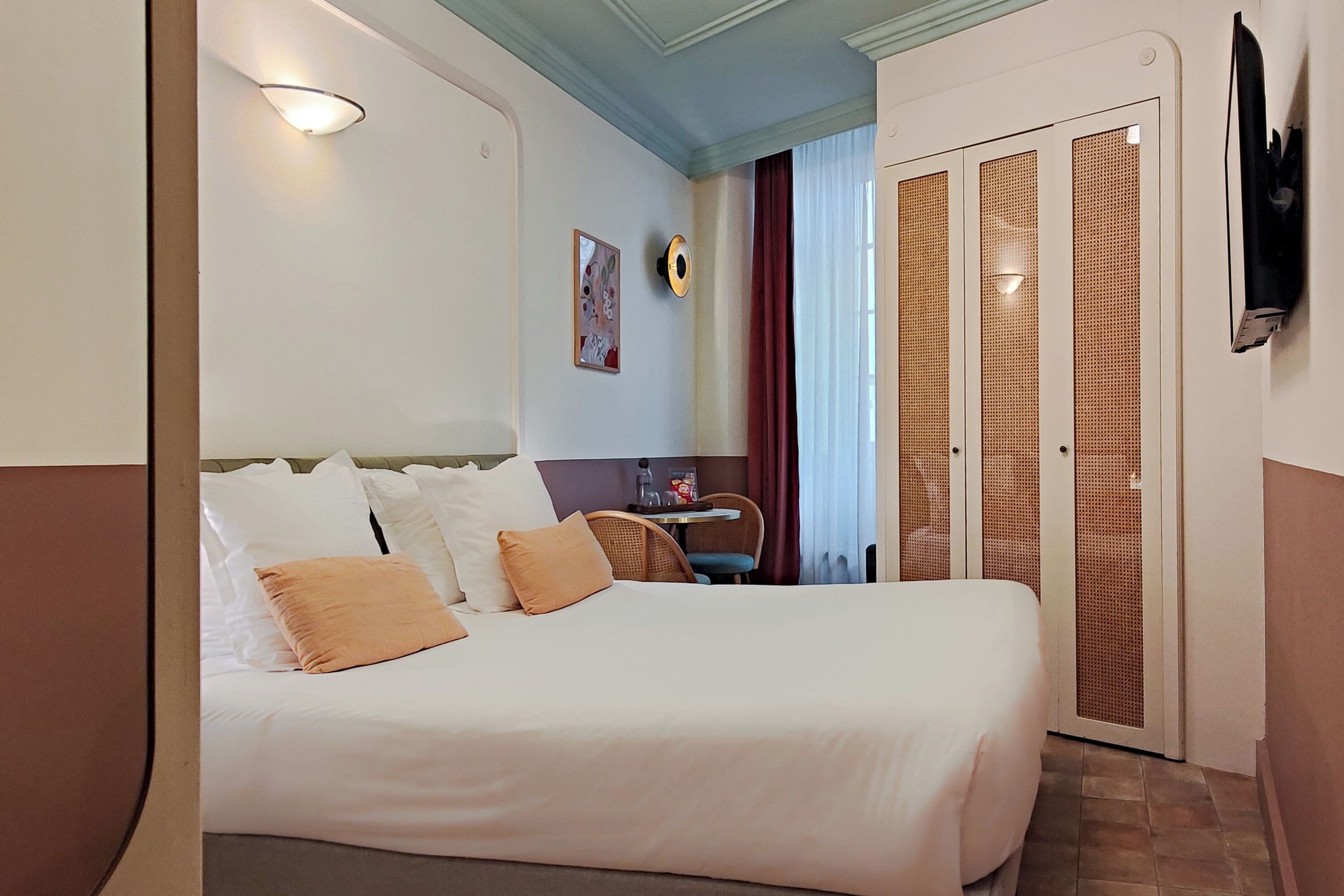 A hotel room with a large bed, a desk, a chair, and a TV mounted on the wall.