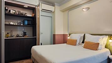 Una habitación de hotel con cama, mesita de noche y una kitchenette con microondas y otros electrodomésticos.