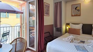 A hotel room with a bed, a chair, a table, a balcony, and a door.