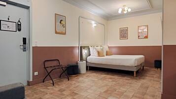 A bedroom with a bed, a chair, a trash bin, and a mirror.