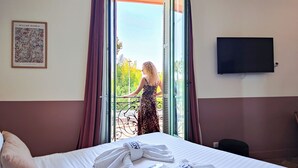 A hotel room with a bed, a TV mounted on the wall, and a balcony with a view of greenery. - Hotel Aparthotel AMMI Vieux Nice (Nice)