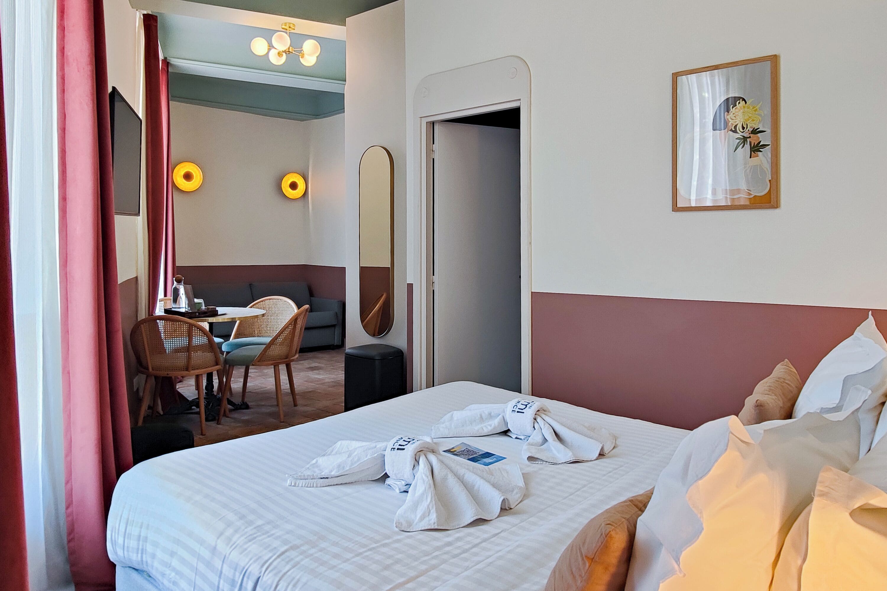 A hotel room with a bed, a desk, chairs, a mirror, and a painting on the wall.