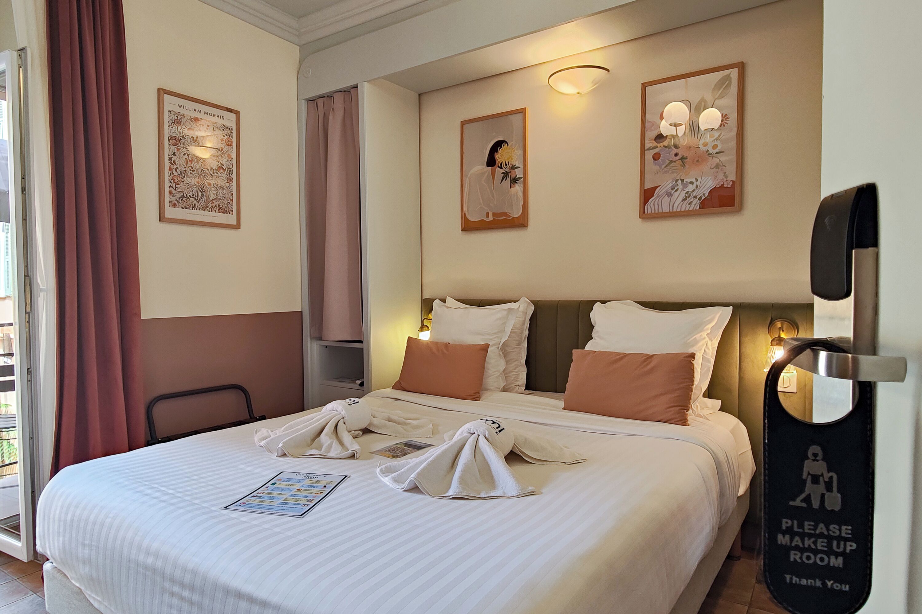 Une chambre d’hôtel avec un lit bien fait, une table de chevet, une lampe fixée au mur et un tableau encadré accroché au mur.