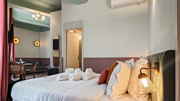 Een hotelkamer met een bed, een bureau, een stoel, een spiegel en een wandairconditioner.