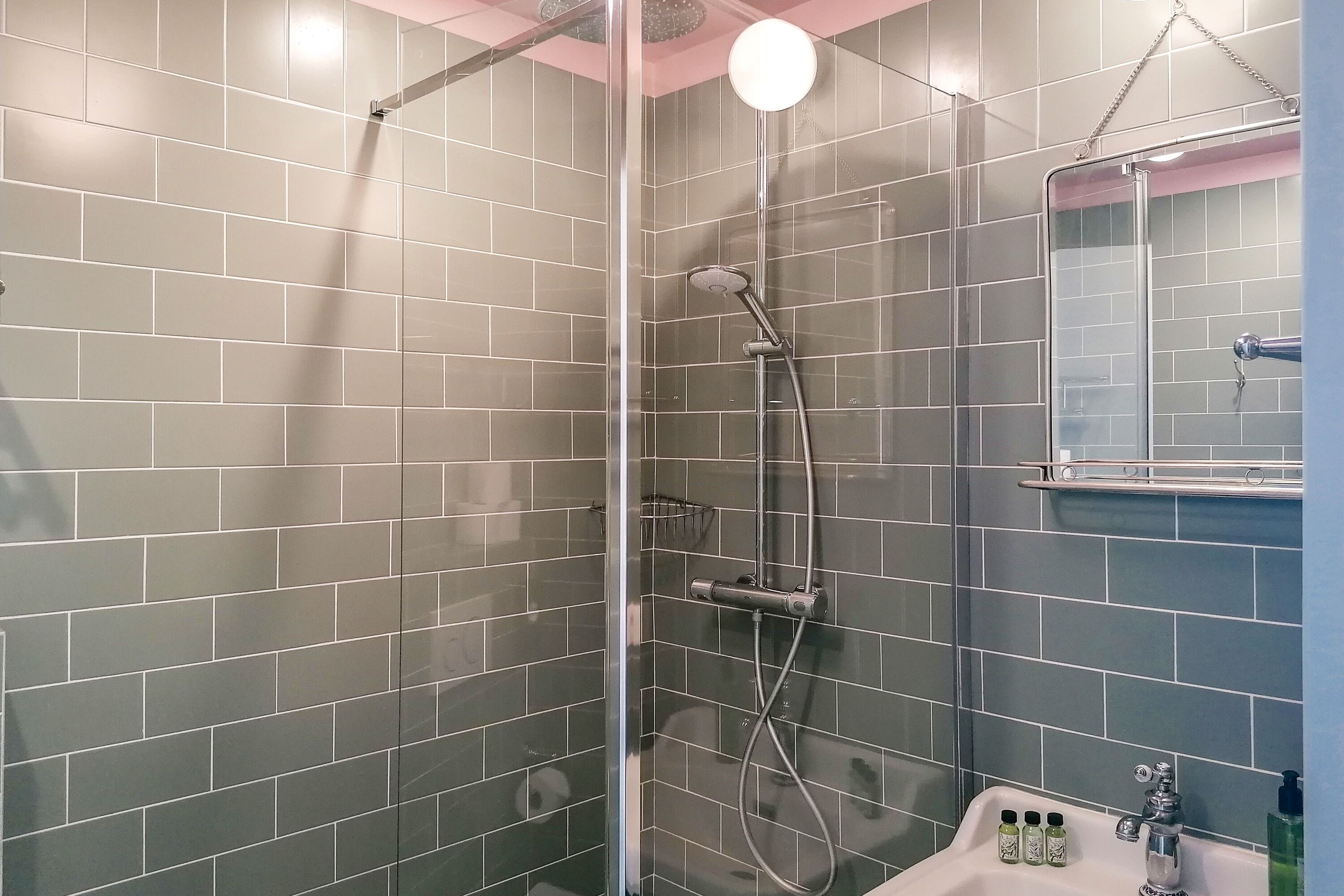 Een badkamer met een glazen douchecabine, een wastafel met spiegel en betegelde wanden.