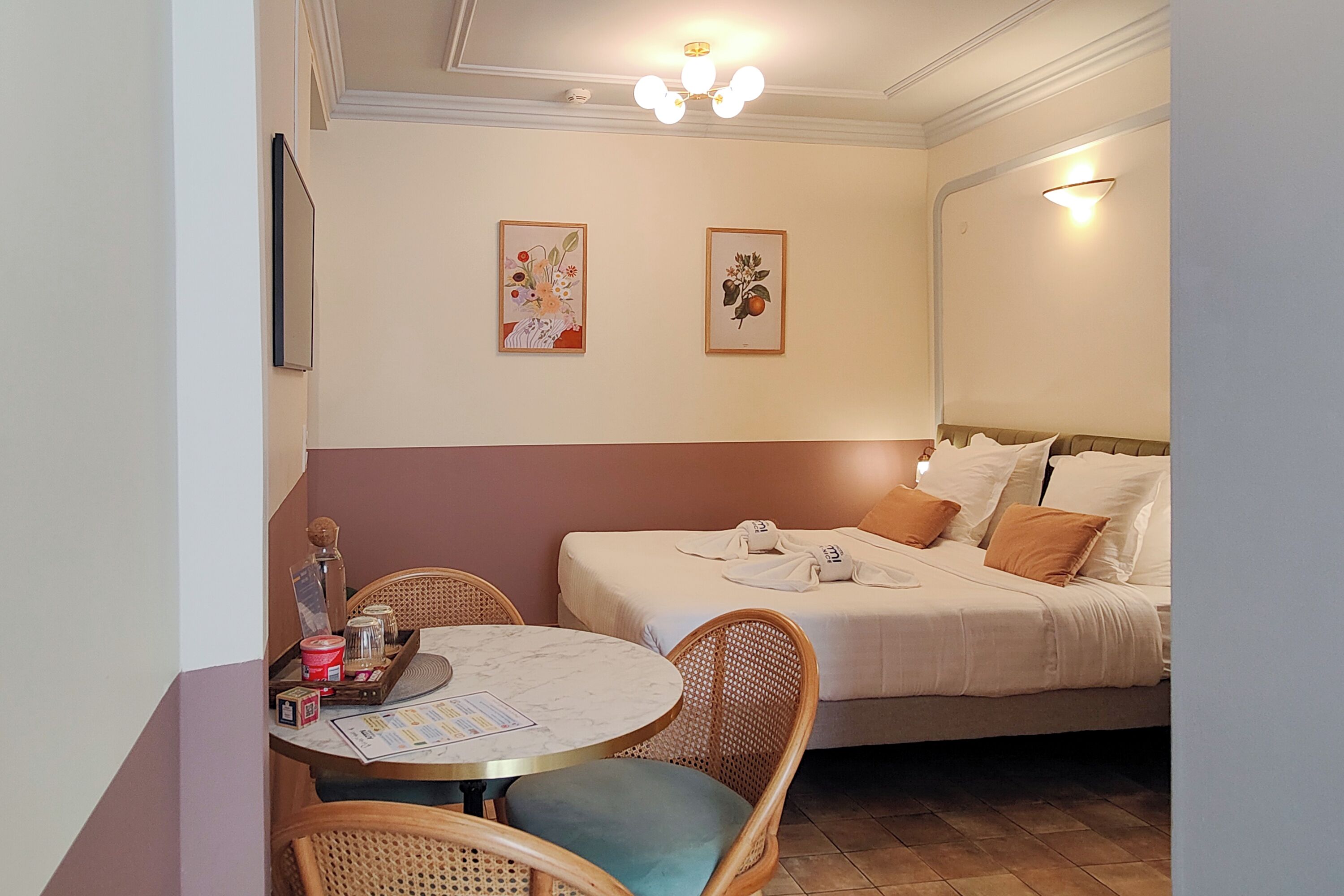 A hotel room with a bed, a round table with chairs, and two framed pictures on the wall.