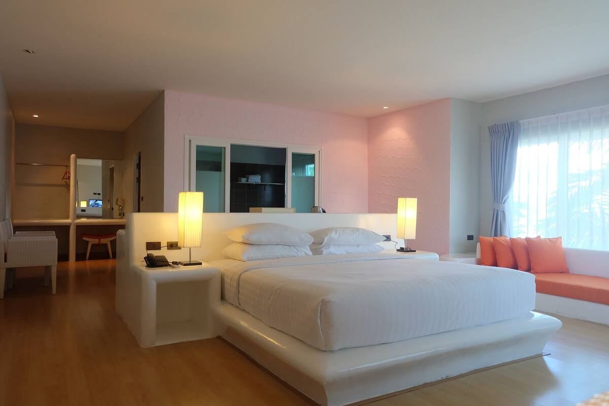 Un dormitorio moderno con una cama grande, mesitas de noche, un escritorio y una zona de estar junto a la ventana.