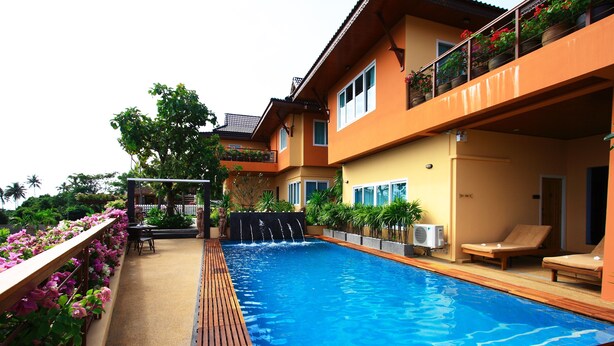 A swimming pool with a wooden deck, surrounded by a building with balconies and potted plants. - The Chalet Phuket Resort (Wichit)