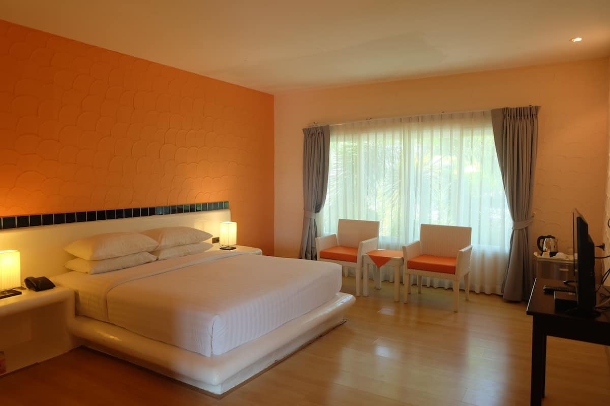 Habitación de hotel con una cama grande, dos sillas, un escritorio con computadora y una ventana con cortinas.
