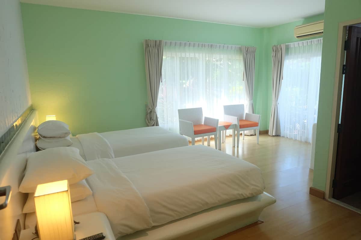 Habitación de hotel con dos camas, un escritorio con sillas y ventanas grandes con cortinas.