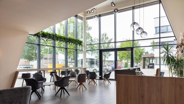 A modern interior with large windows, black chairs, and a wooden reception desk. - Dominik Motel (Paderborn)