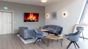 A modern lounge area with a fireplace, grey upholstered seating, a round coffee table, and wall-mounted lighting. - Dominik Motel (Paderborn)