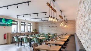 A modern restaurant with a long counter, green upholstered chairs, and a wooden wall with a clock. - Dominik Motel (Paderborn)