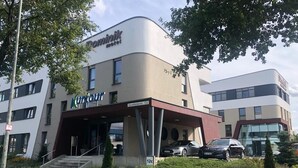 A modern hotel with a covered entrance, a car parking area, and a building with a sign that reads "Dominik Hotel". - Dominik Motel (Paderborn)
