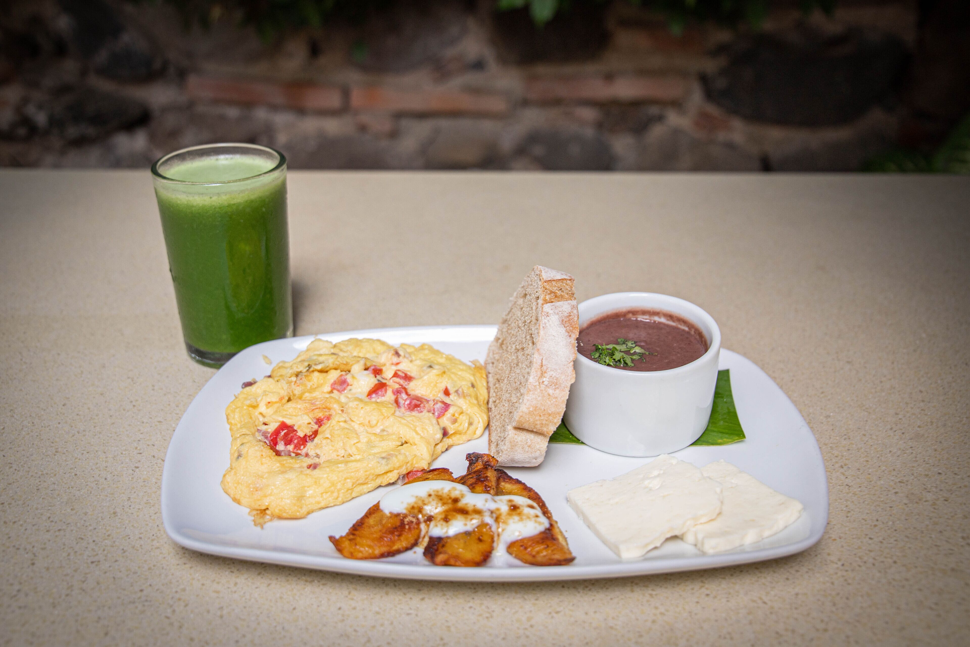 A plate with scrambled eggs, toast, a bowl of soup, and a glass of green smoothie.