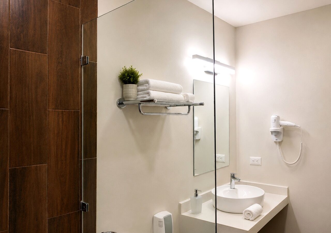 A modern bathroom with a glass shower enclosure, a white sink, a towel rack, and a hairdryer.