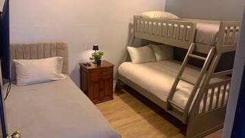 Un dormitorio con una cama litera, una cama individual, una mesita de noche con lámpara y una planta pequeña.