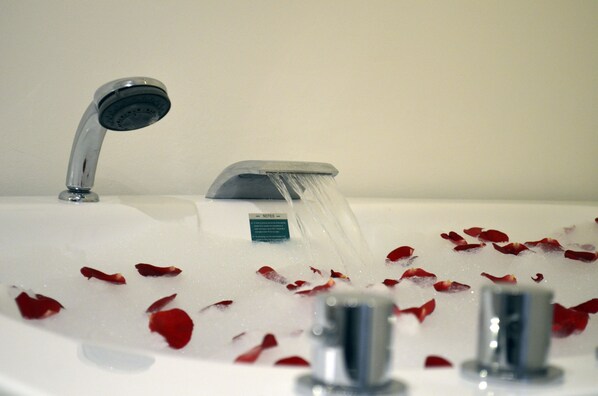 A bathroom with a bathtub filled with water and rose petals.
