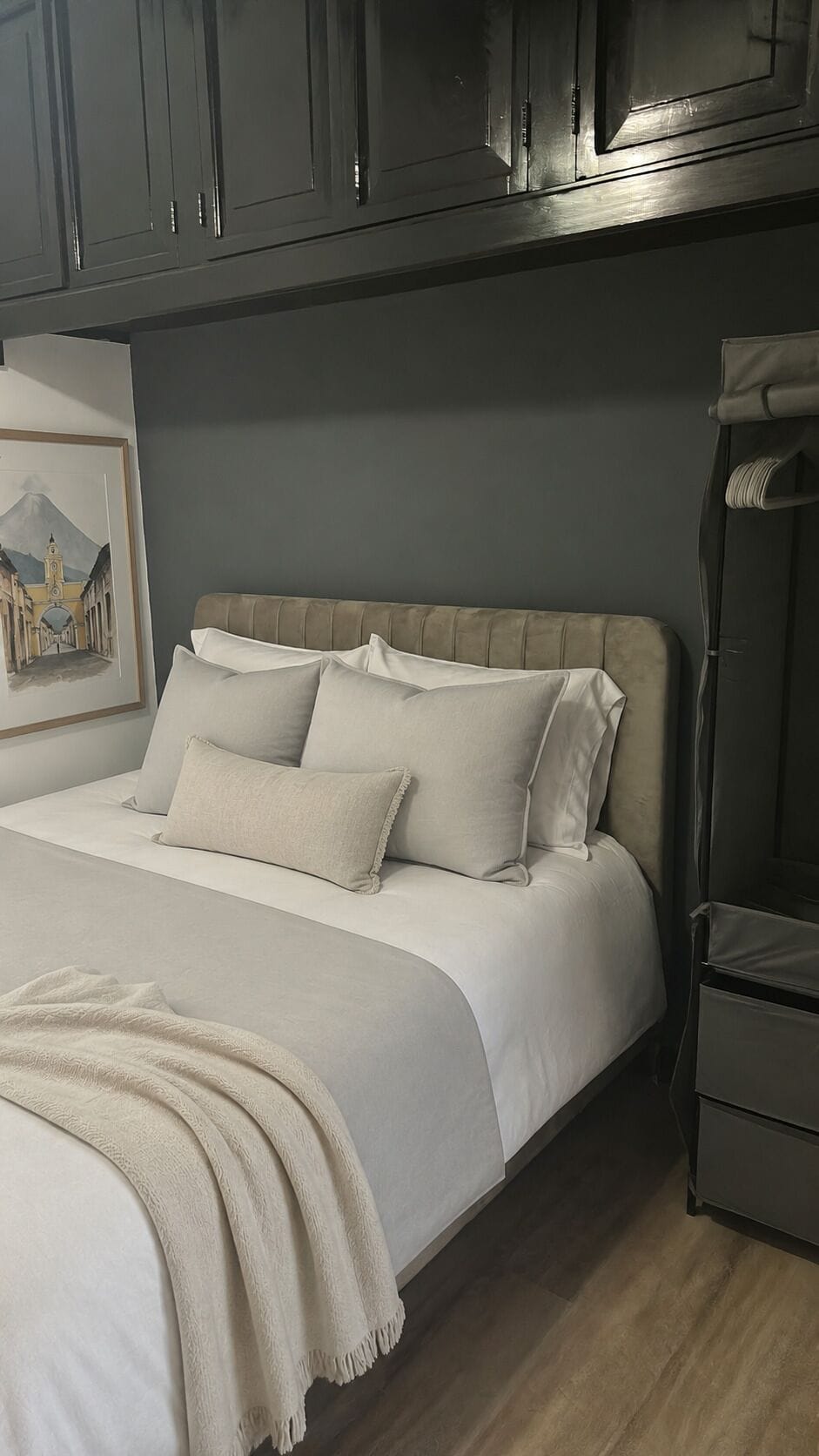 Een slaapkamer met een bed, kussens, een dekbed, een lijst met een afbeelding en een garderobe.