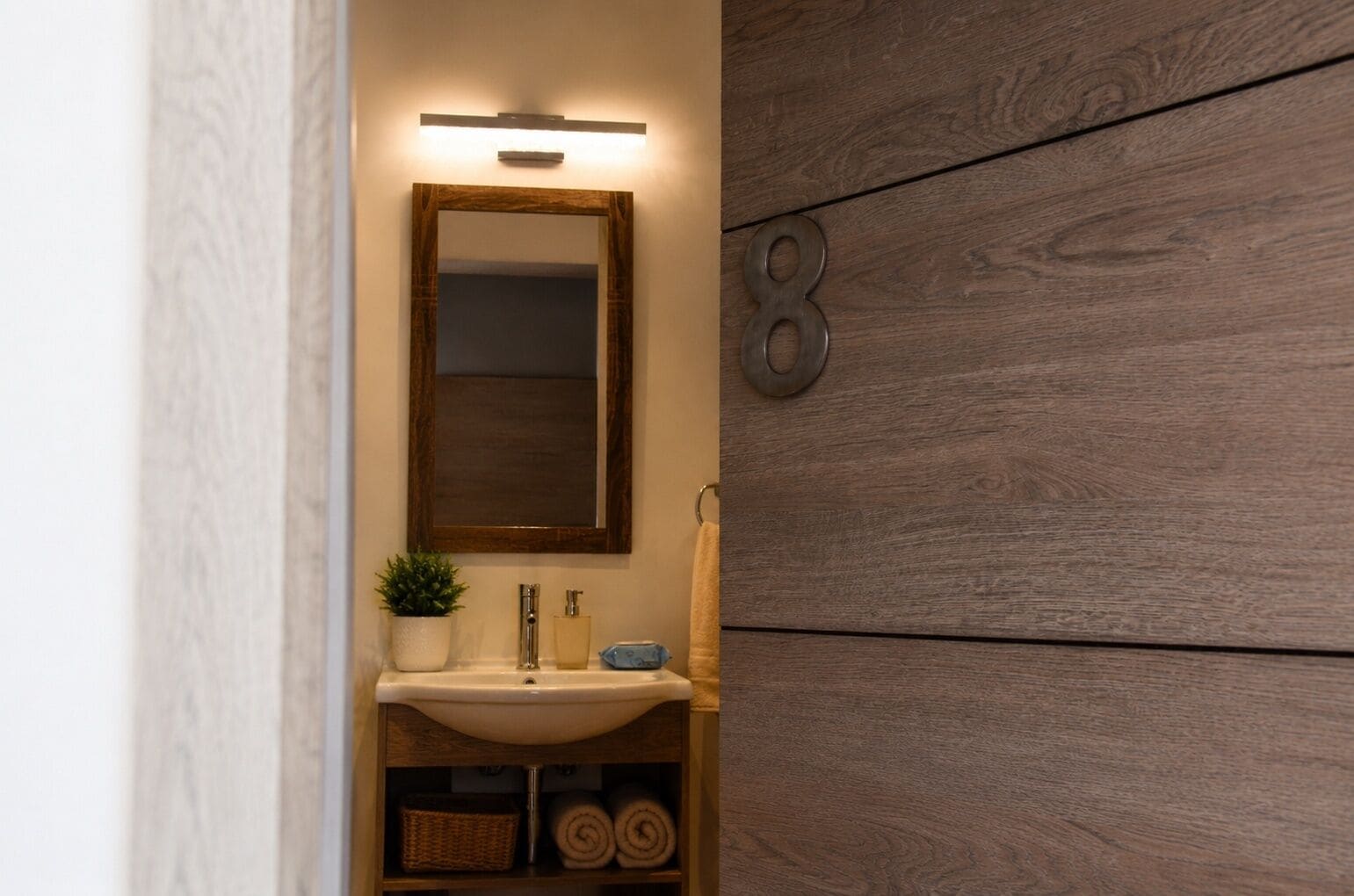 Un baño con tocador de madera, un espejo, un lavabo, una planta en maceta y un perchero para toallas.